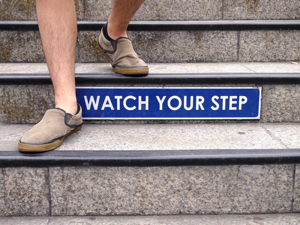 Photo of Watch your step sign on a staircase and a pair of feet with shoes
